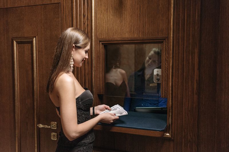 A woman in a black dress holding cash at a cashier's window in a wooden interior.