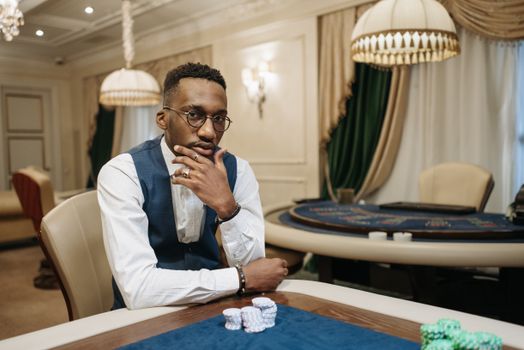 A contemplative man sits at a casino table with poker chips, exuding sophistication and focus.