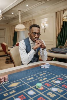 Focused man strategizing at a casino gaming table surrounded by poker chips.