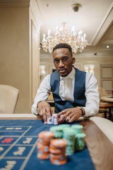 An African American man confidently gambling at a luxurious casino with stacked chips and elegant surroundings.