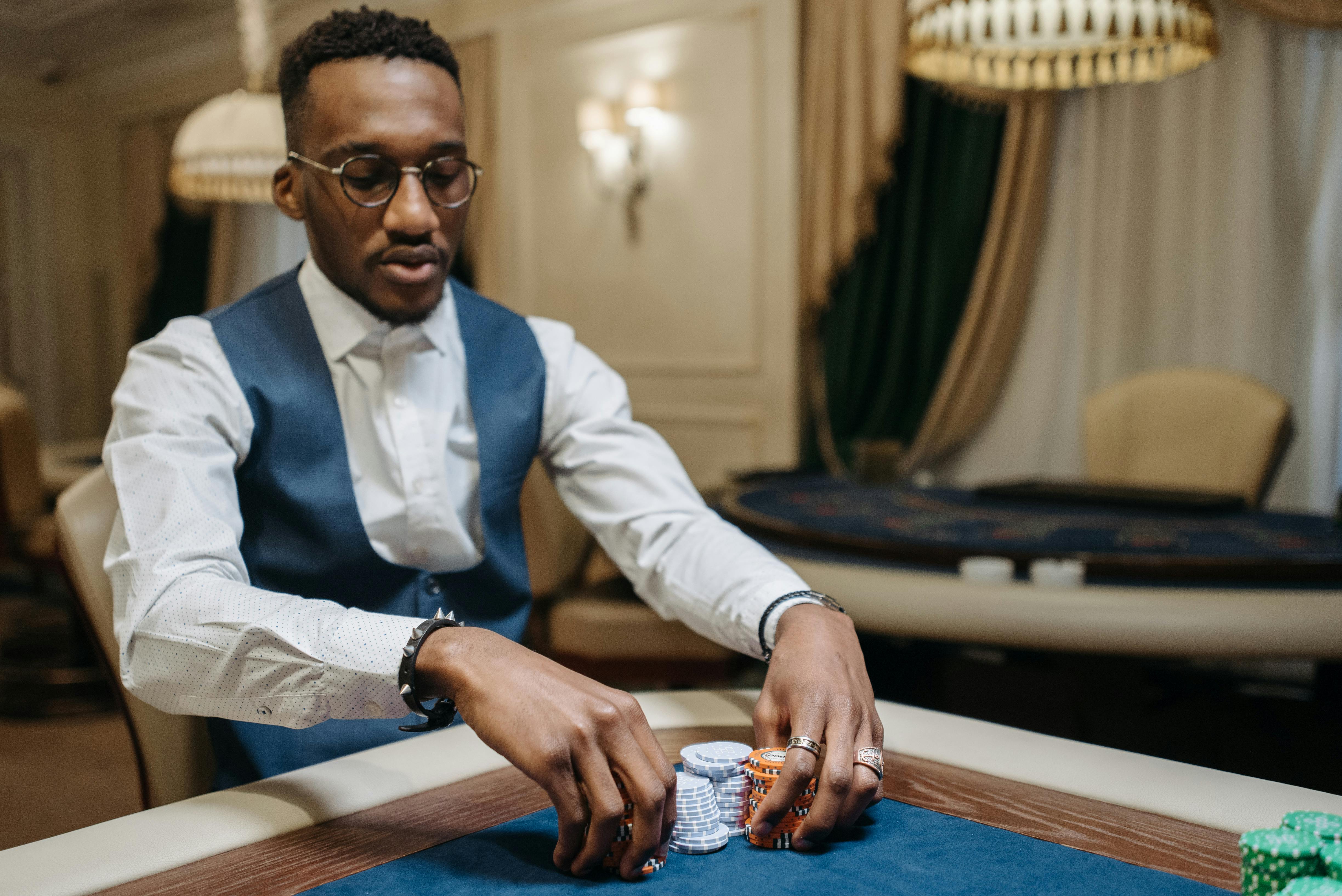 a man wearing eyeglasses sitting at a table holding stacks of casino tokens