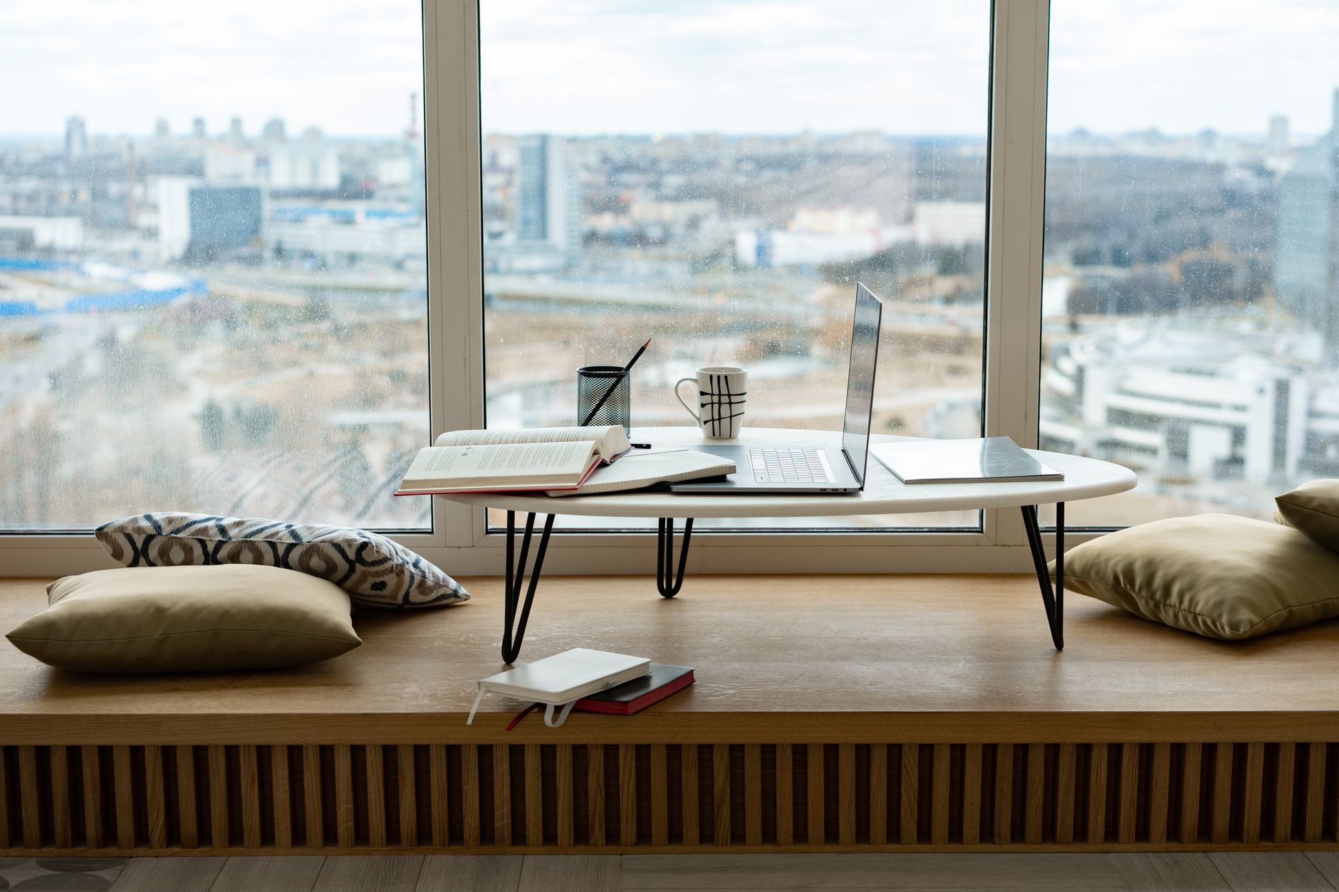 A coffee cup and an open notebook on a wooden table beside a window during a midday break