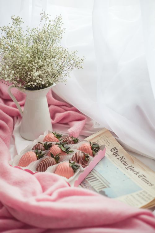 Free A serene still life featuring baby's breath, chocolates, and a newspaper on pink fabric. Stock Photo