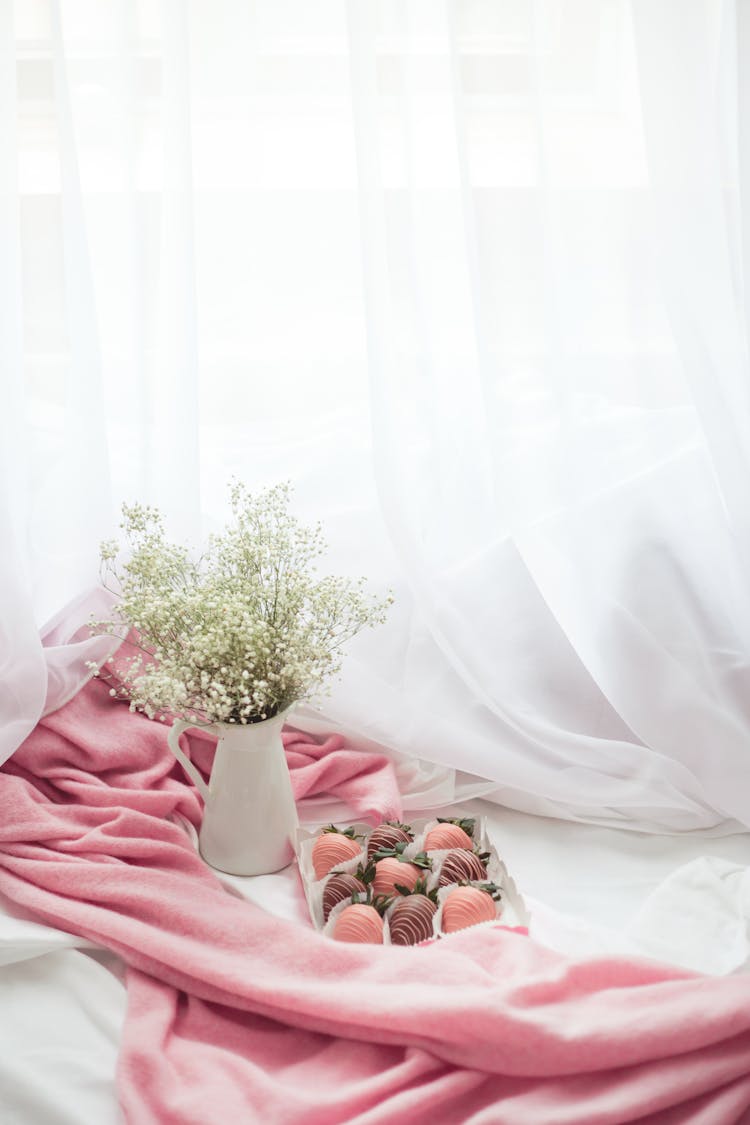 Chocolates Beside A Pink Cashmere Scarf And A Vase Of Baby's Breath Flowers