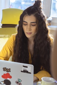 Focused woman with long hair working on a laptop in a bright indoor setting.