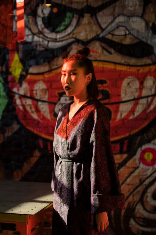 Free Fashionable woman in kimono standing before vibrant graffiti wall in urban setting. Stock Photo
