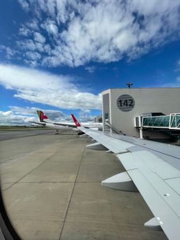 Airplane wing view at the airport gate, clear blue sky above. Ideal for travel and aviation themes.