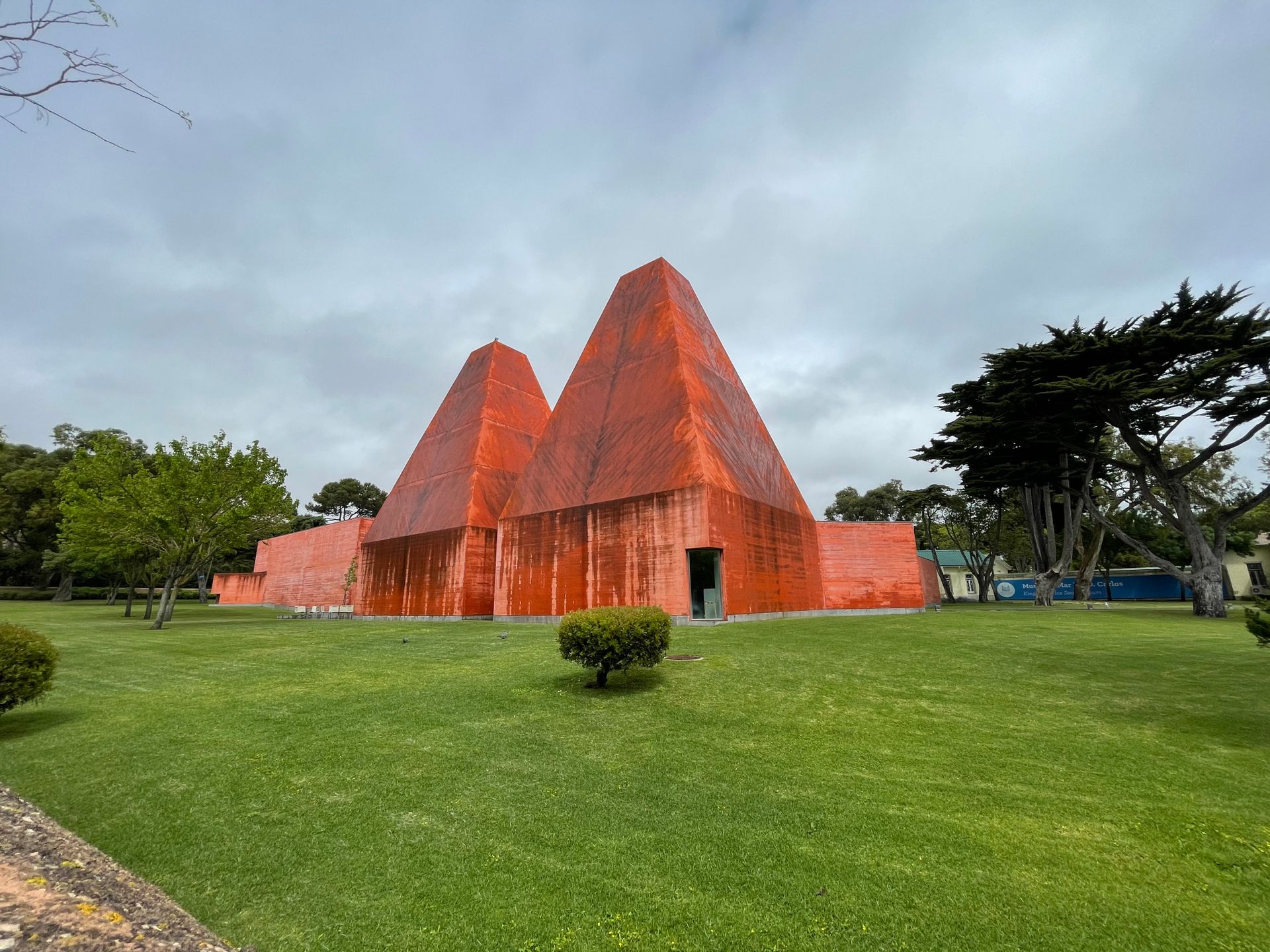 Modern architecture of Casa das Histórias Paula Rego museum set amid green lawns and trees under a cloudy sky.