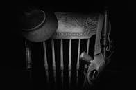 这是一幅经典的西部主题黑白静物画，画中有帽子、木椅和枪