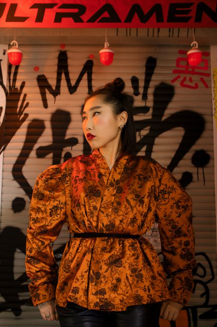 Fashionable woman in orange kimono-style jacket posed against vibrant graffiti at night.