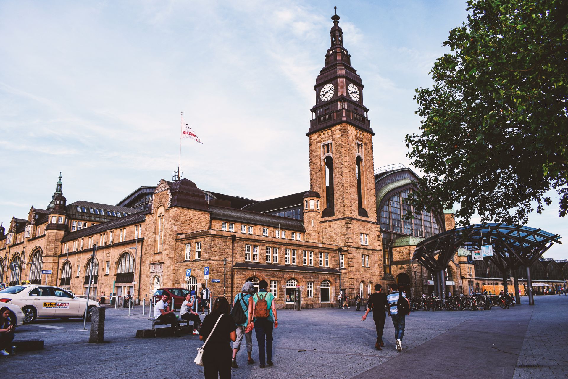 Dynamic scene at Hamburg Central Station with people and iconic architecture under a blue sky.