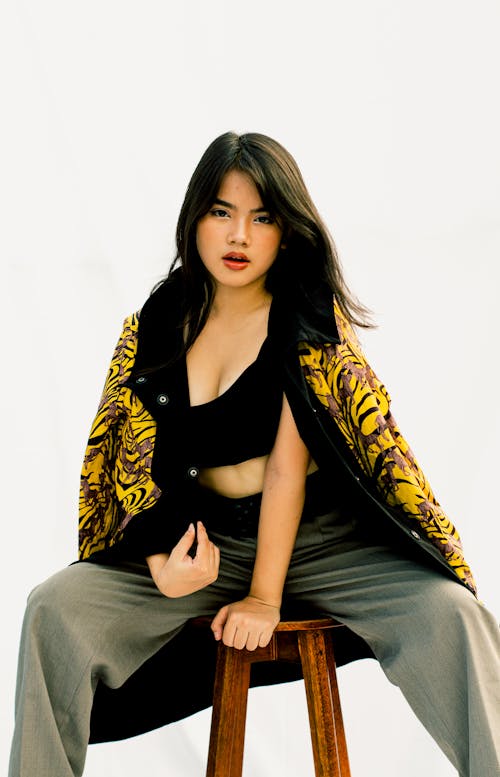 A Woman Wearing Black Crop Top and Yellow Jacket Sitting on a Bar Stool