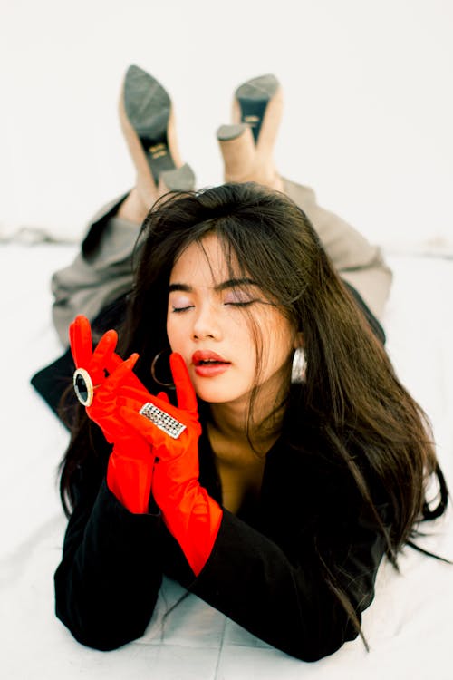 Woman in Black Long Sleeve Shirt and Red Gloves Lying on White Surface in Prone Position