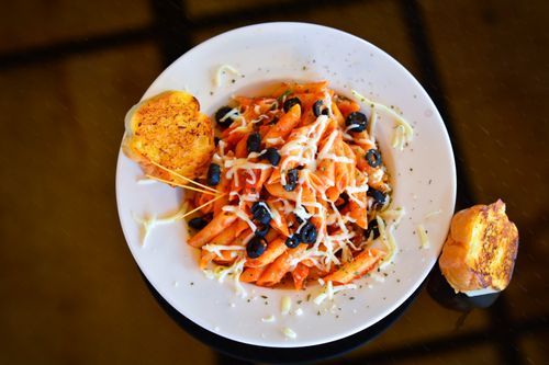 Free A vibrant plate of penne pasta topped with olives and cheese, garnished with bread on the side. Stock Photo