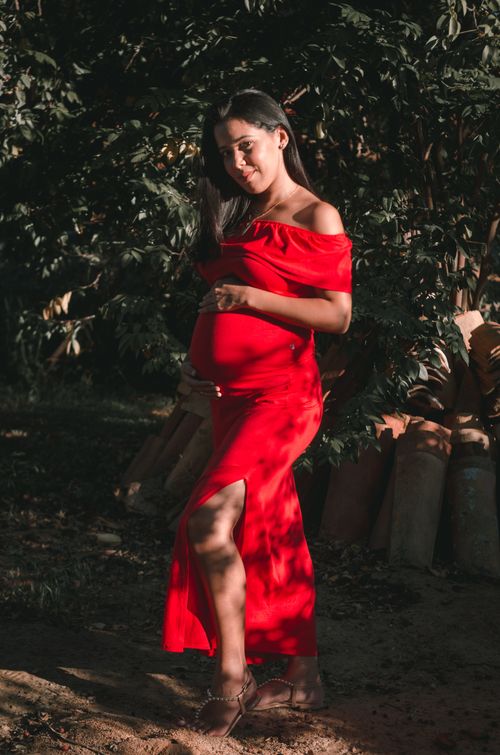 Free A pregnant woman poses confidently outdoors in a stylish red dress, accentuating her baby bump. Stock Photo