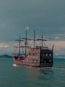 A classic wooden ship sails on a calm ocean under a partly cloudy sky.