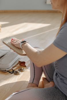 A woman meditates in lotus position using a sadhu board for alternative therapy indoors.