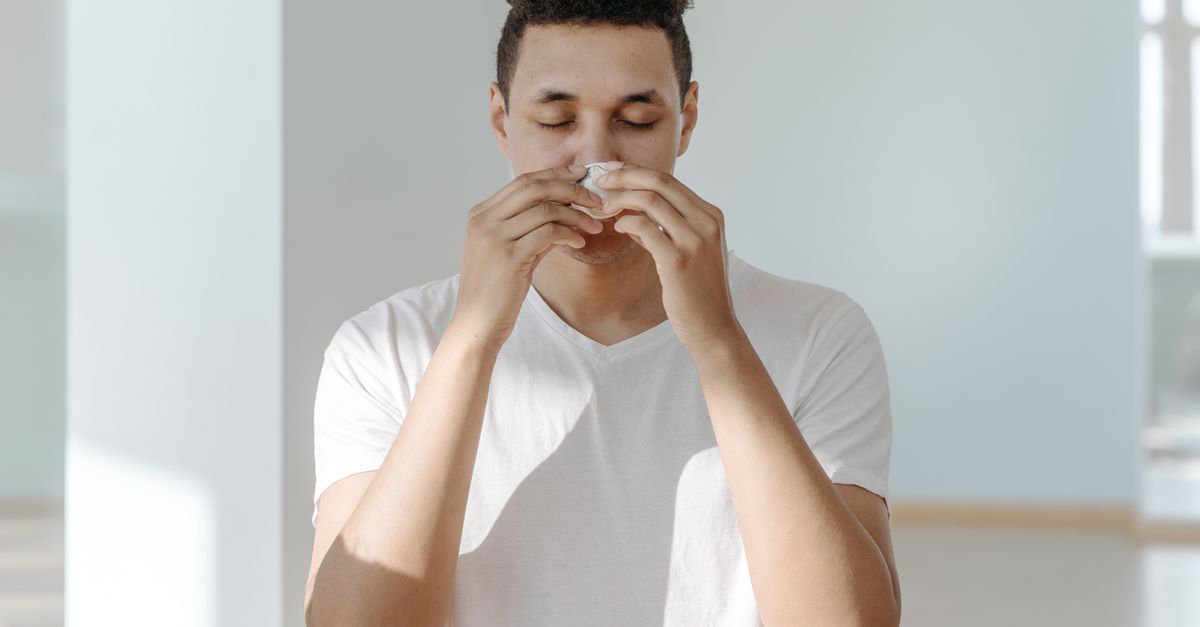 A man sneezing into a tissue, illustrating symptoms of flu or allergies. - Evidence evidence guide for vitamin d respiratory infection meta-analysis