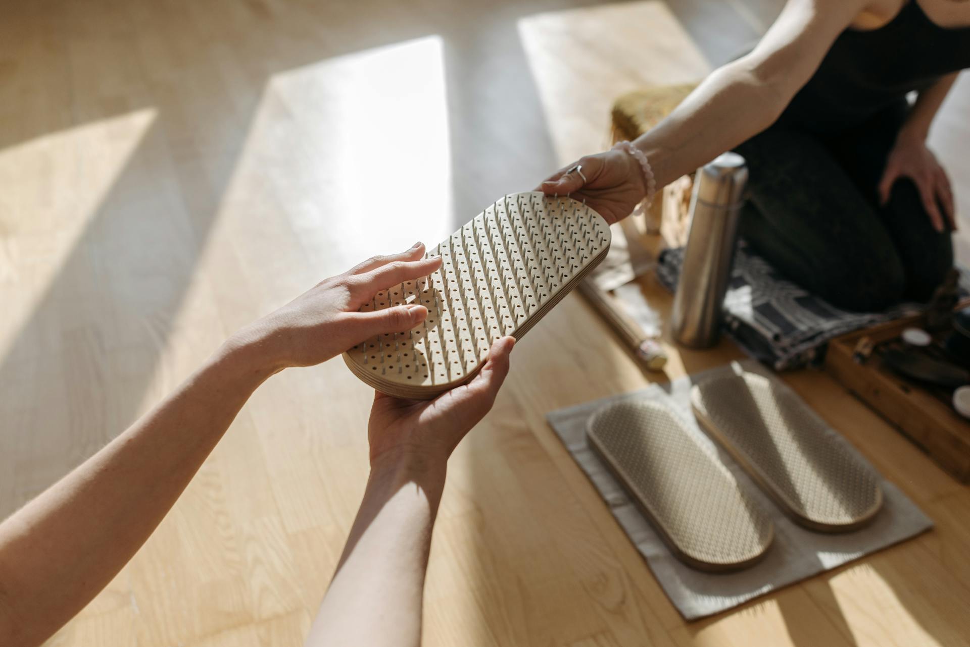 Hands exchanging a wooden acupressure board over a smooth wooden floor indoors, depicting relaxation and wellness.