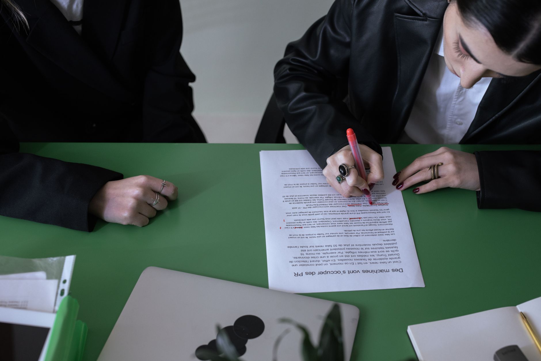 A woman marking a document with a red pen at a green desk.