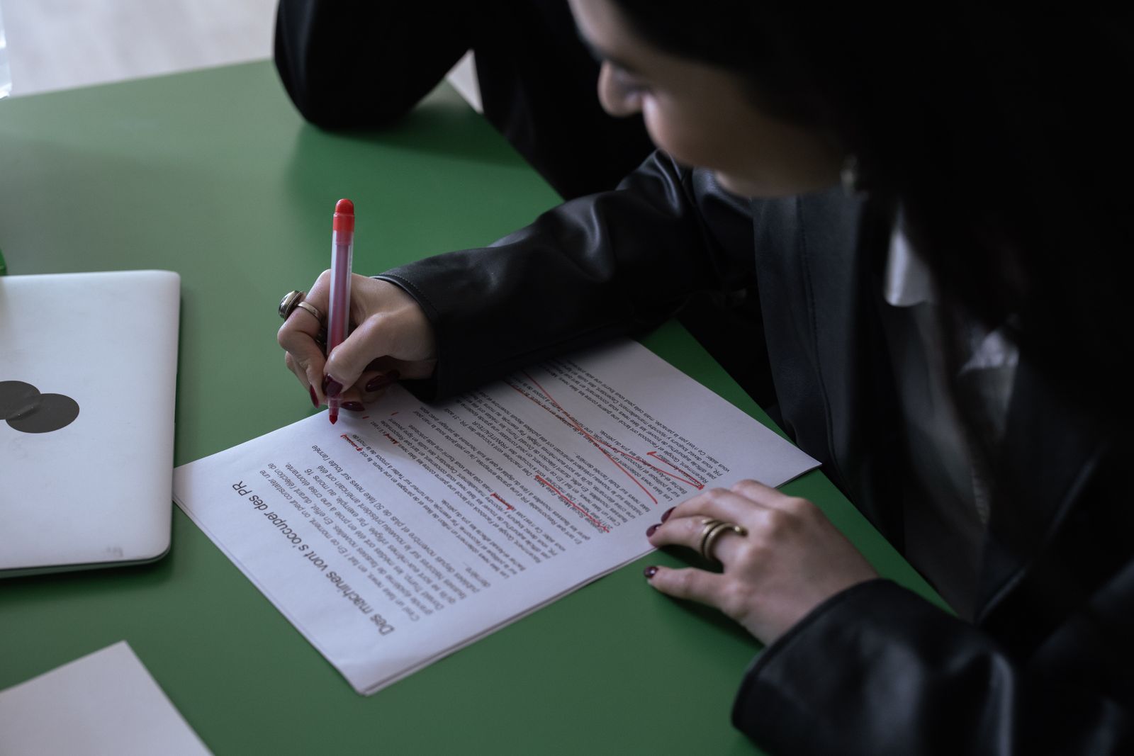 Professionnelle corrigeant un document imprimé au stylo rouge près d’un ordinateur