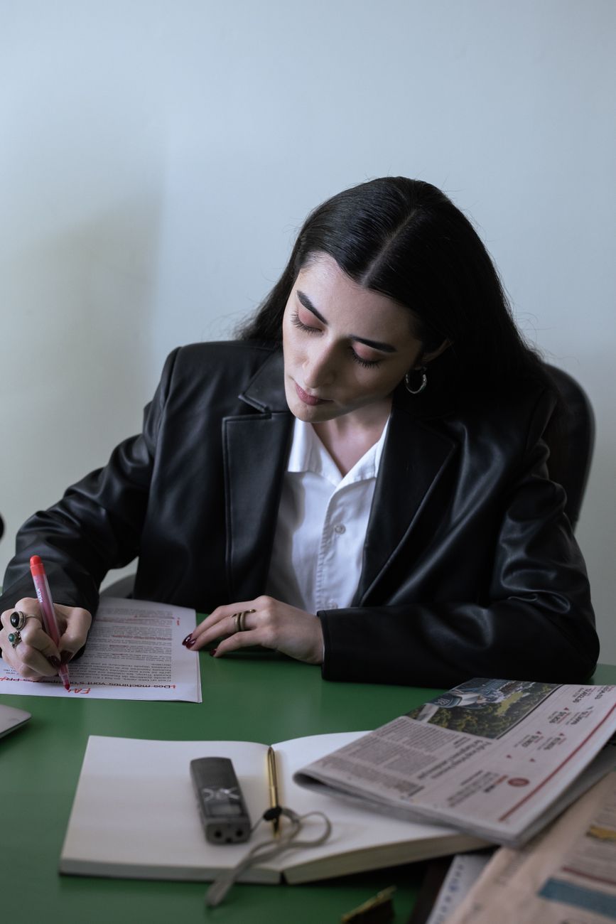 A professional woman in a black blazer reviews paperwork at her workspace.