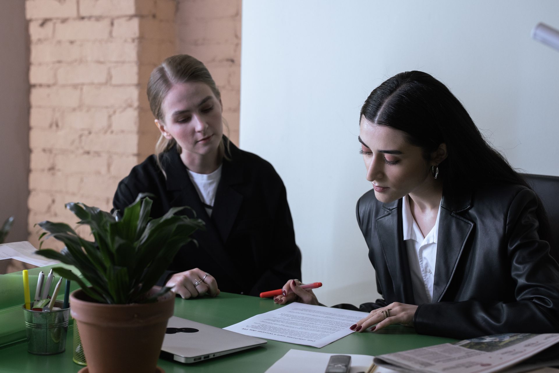 Two women collaborate in a modern office, reviewing documents at a desk.