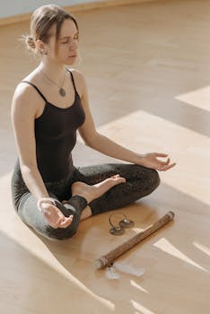 Serene woman practicing yoga in lotus position with eyes closed on a sunlit wooden floor.