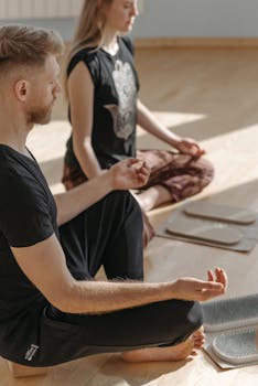 Two adults meditating indoors on wooden flooring in a wellness session.