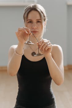 A woman standing indoors holding traditional meditation cymbals in a bright setting.