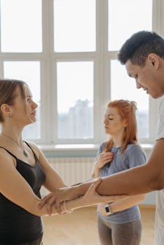 Three individuals engage in a yoga practice, focusing on connection and mindfulness in an indoor studio setting.