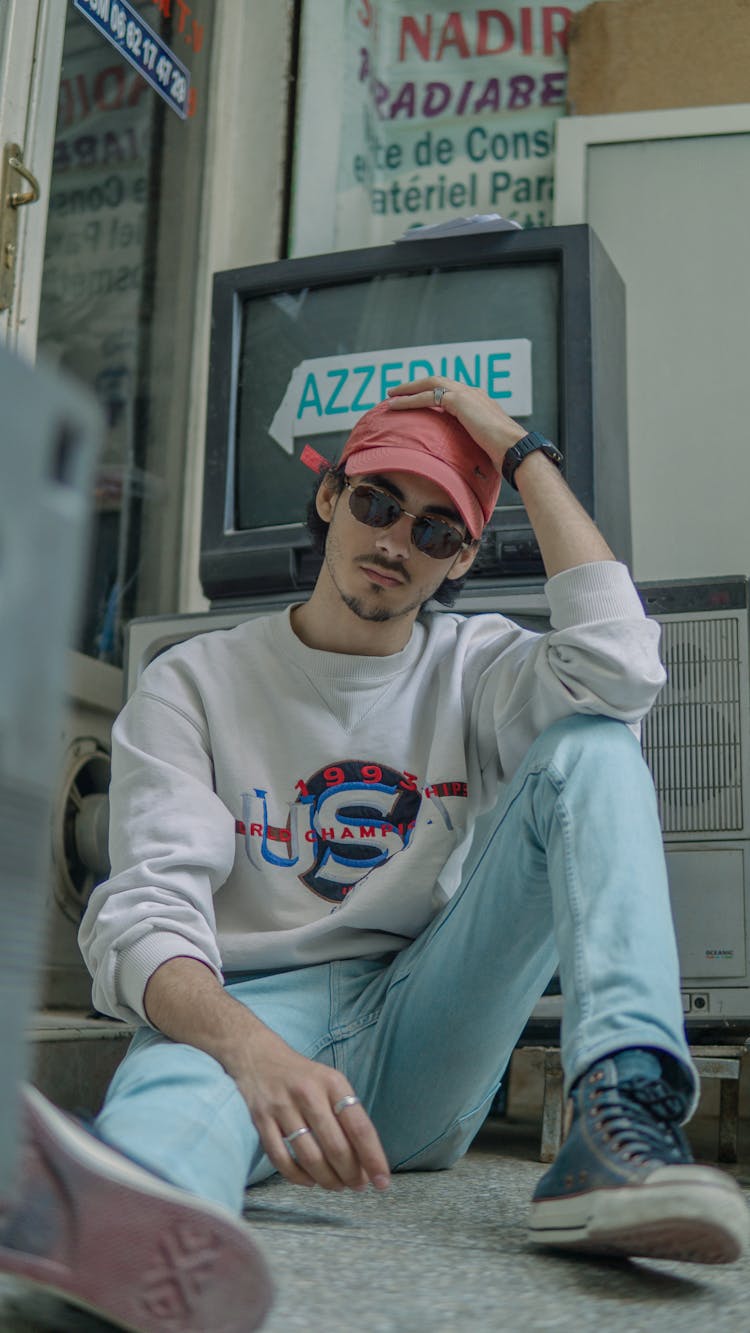 Man Wearing A Gray Sweater Sitting Beside A Vintage Television