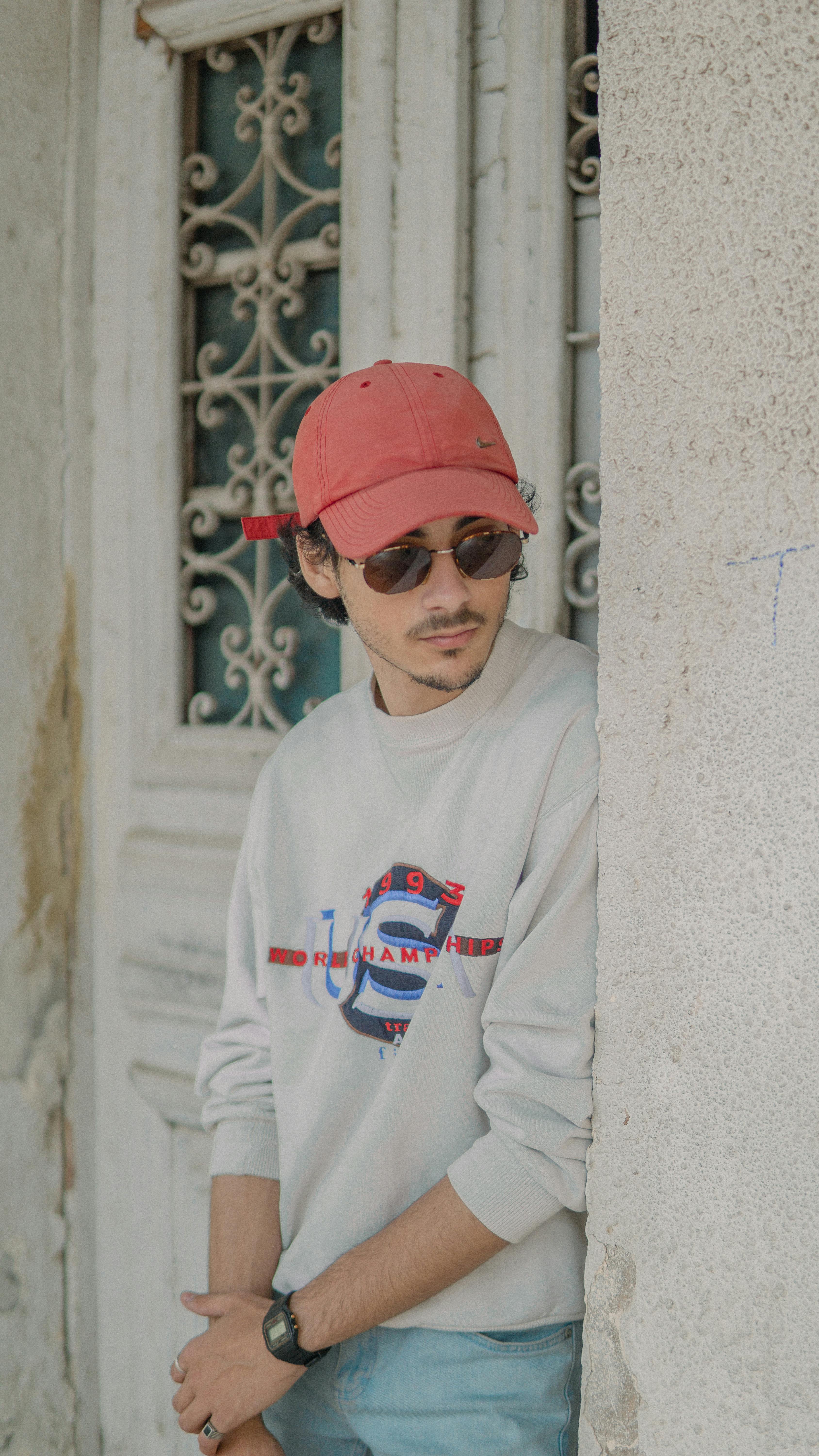 Young man in casual wear leaning against a wall in Fes, Morocco, wearing a cap and sunglasses.