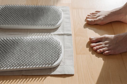 A pair of bare feet near a metal sadhu board on a wooden floor for therapeutic use