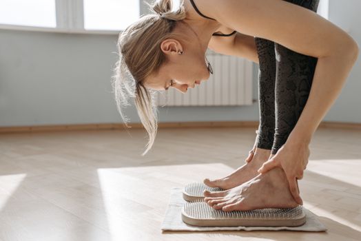 A woman performs a yoga pose on a sadhu board in a bright indoor setting, promoting wellness.