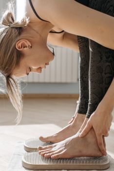 A woman performing a yoga pose on a sadhu acupressure board indoors, promoting relaxation.