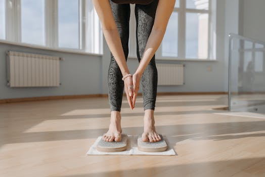 An adult woman performs yoga on a sadhu board indoors, focusing on balance and mindfulness.