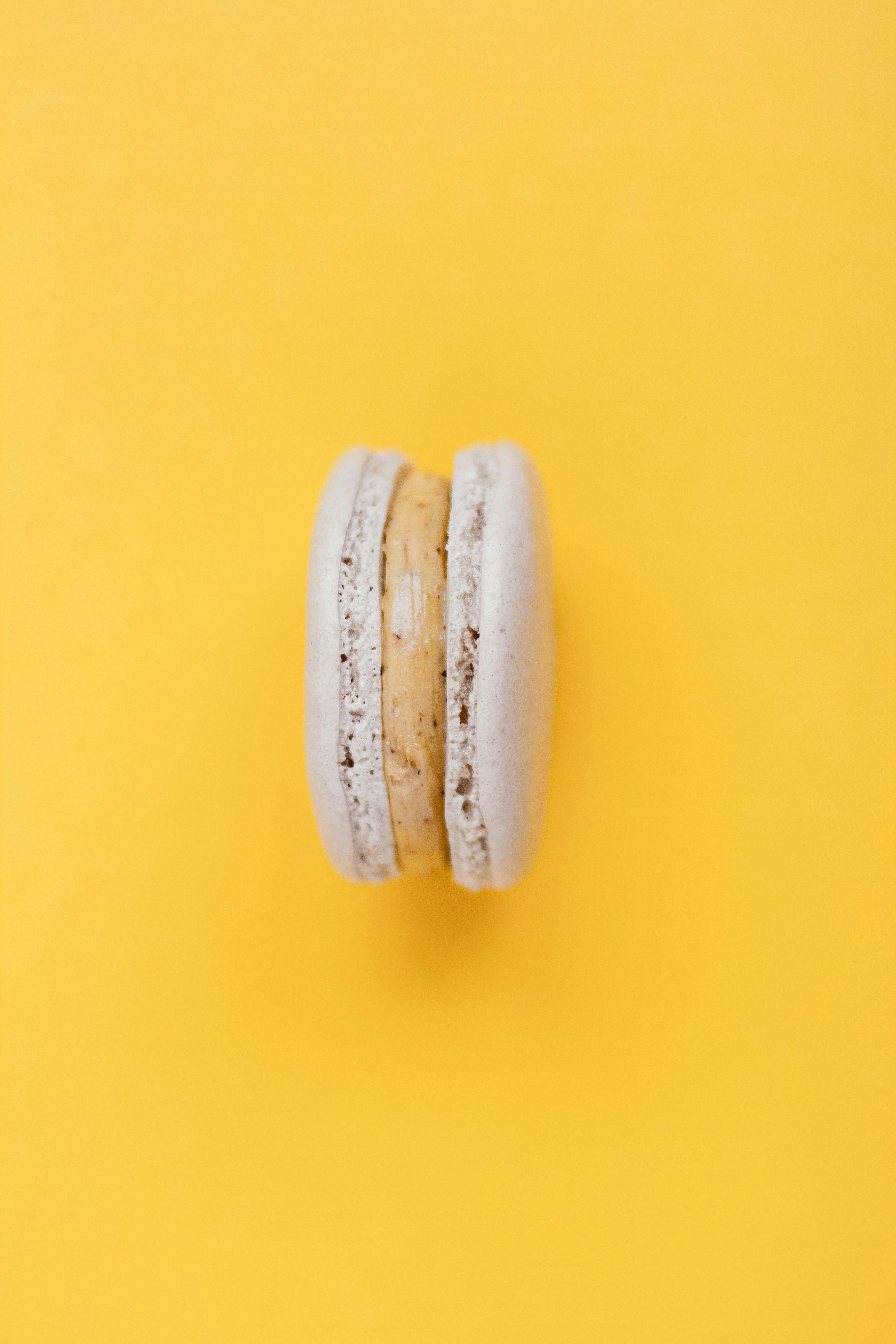 Top view of tasty sweet white macaroon with delicious cream placed on yellow background