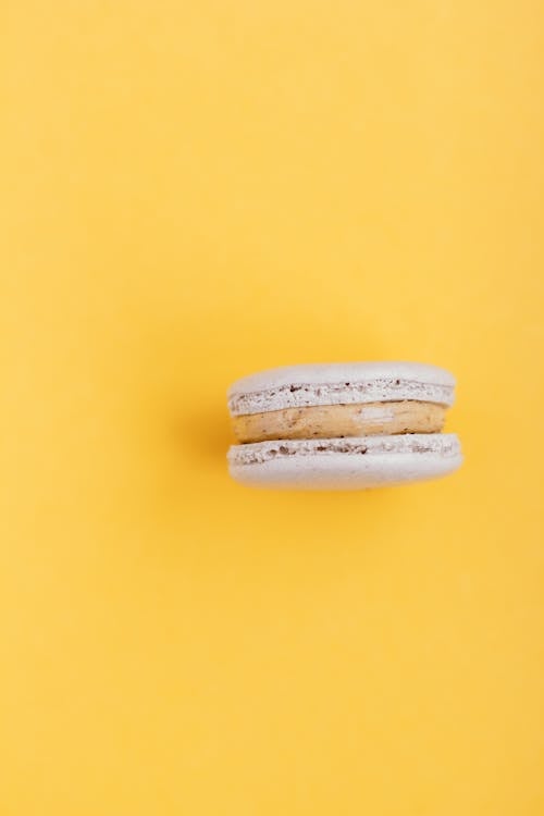Top view of tasty sweet macaroon with cream placed on yellow surface in studio
