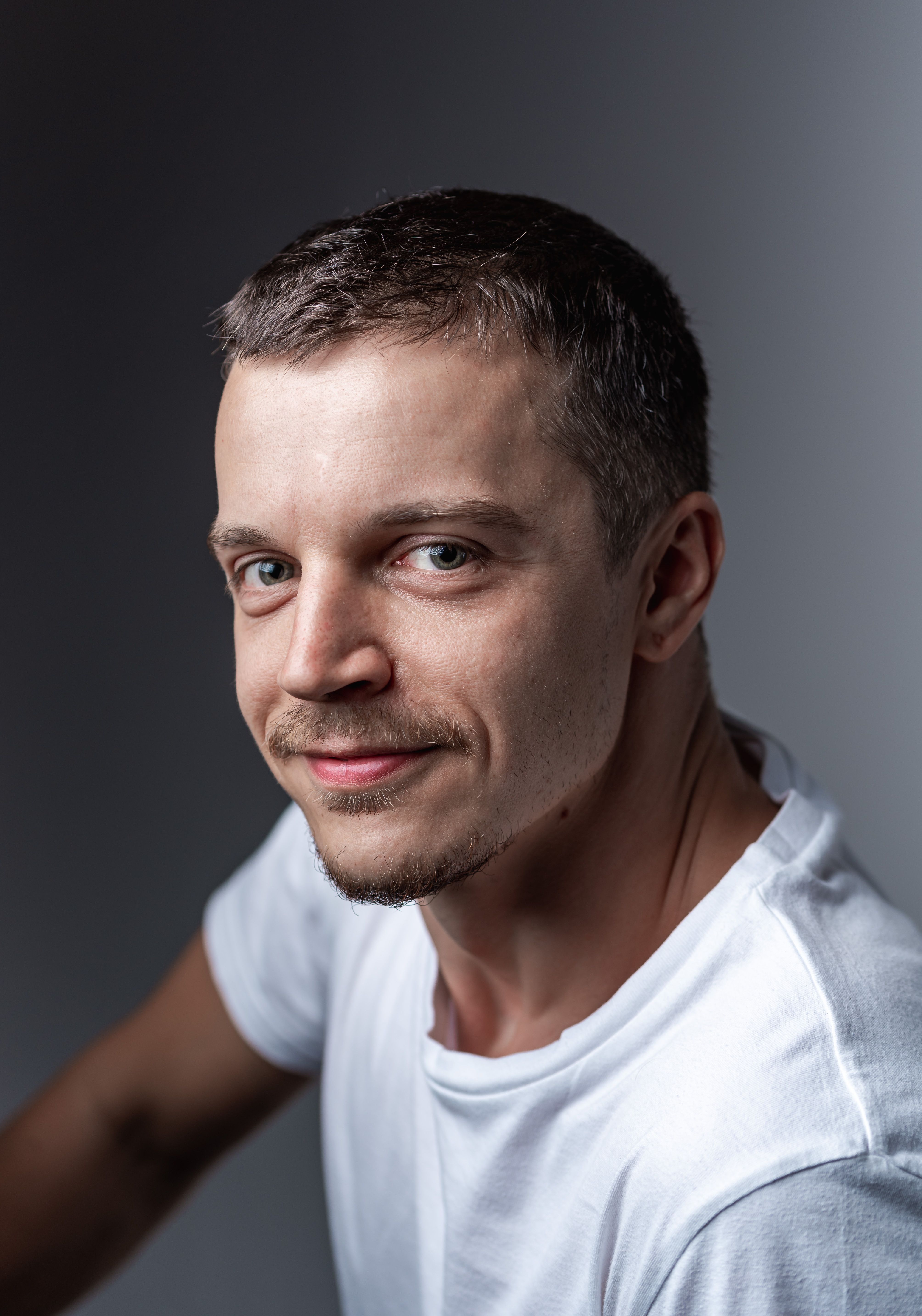 Engaging close-up portrait of a smiling man wearing a white shirt against a neutral background.
