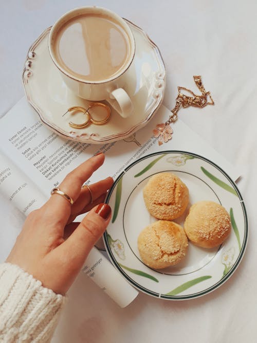 A Hand Touching the Saucer with Breads Near a Cup of  Coffee 