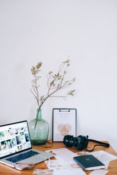 A serene minimalist workspace featuring a laptop, camera, and decorative vase with branches.
