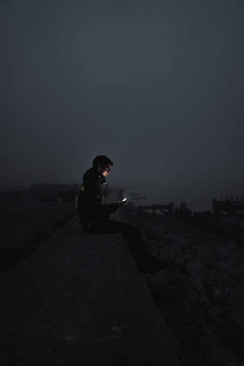 A Man Sitting on the Seawall at Night · Free Stock Photo