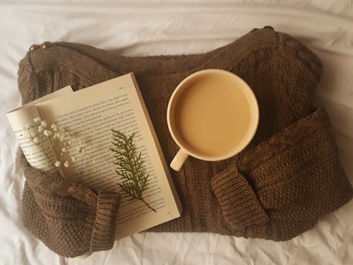 A Cup of Coffee and an Open Book over a Knitted Sweater