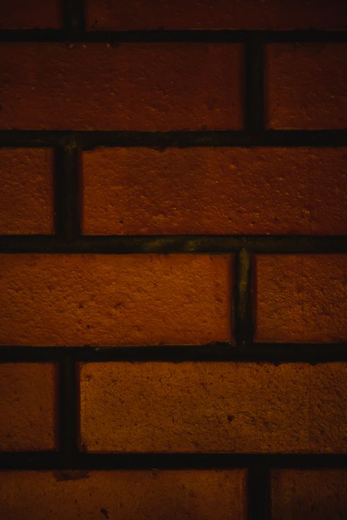 Free Detailed close-up of a rustic brick wall texture in dim lighting, highlighting earthy tones. Stock Photo