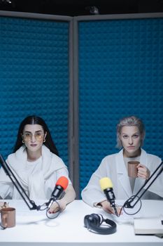 Two women in a soundproof studio holding coffee cups, engaged in recording.