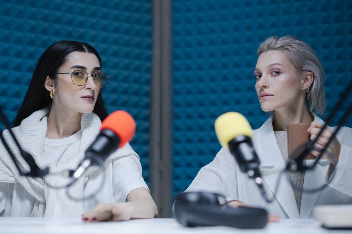 Two hosts at colourful microphones in a blue soundproof studio