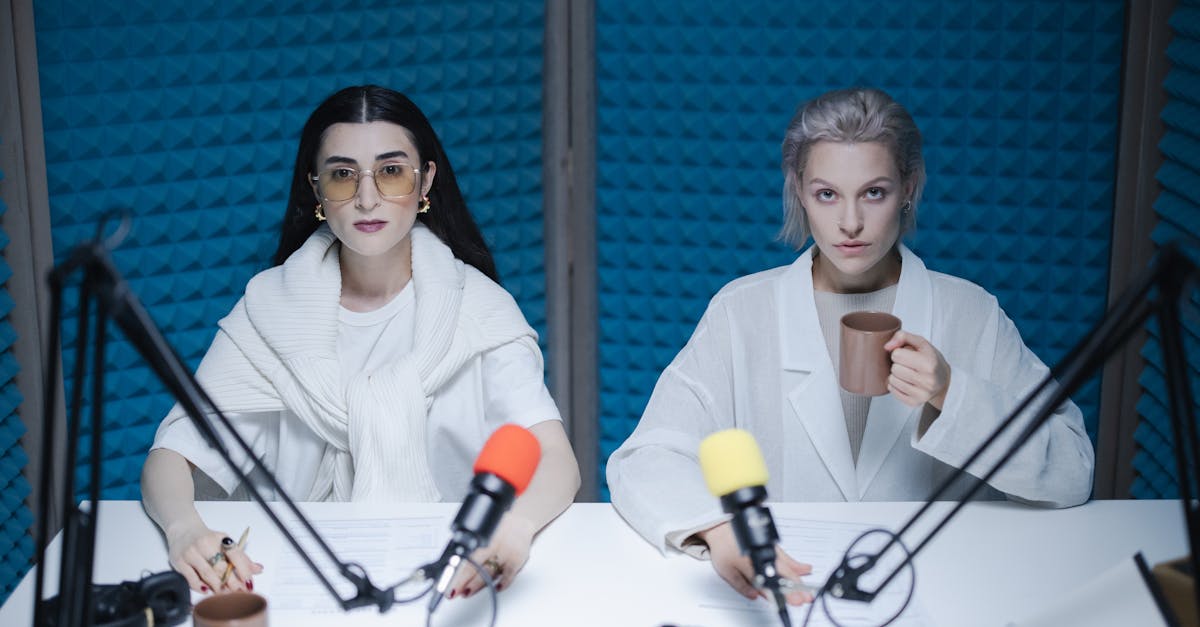 Two women hosting a podcast in a soundproof studio with microphones and coffee.