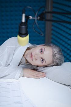 Portrait of a woman in a recording studio, lying on a table with a microphone overhead.