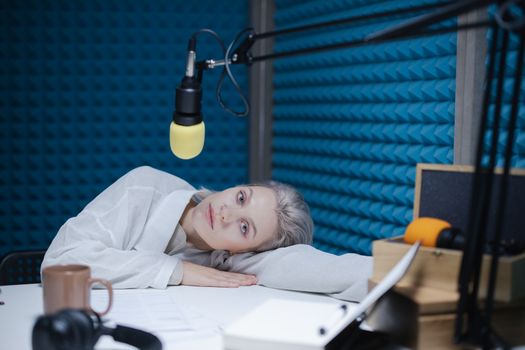 A woman laying on a table in a studio with a microphone and soundproofing panels. Relaxed ambiance.